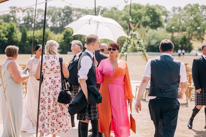 9 Top Tips For Coping With Hot Weather. Guests mingling at wedding reception. Lady in pink and red dress with a white parasol to keep cool.