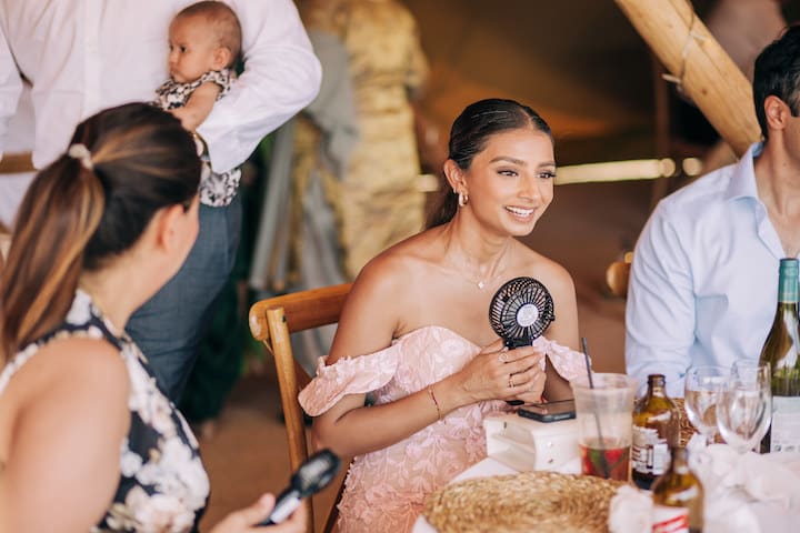 9 Top Tips For Coping With Hot Weather. Female guest sat at a table inside the tipi holding a black electric handheld fan