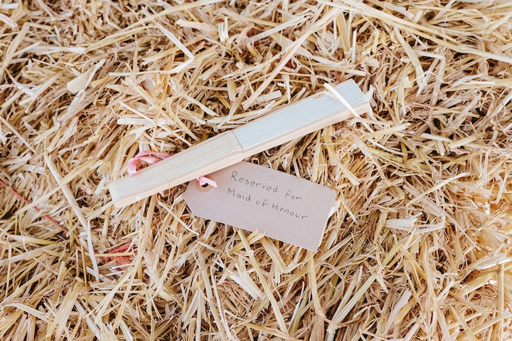 9 Top Tips For Coping With Hot Weather. A paper fan with a tag that reads "Reserved for the maid of honour", sat on a bale of straw