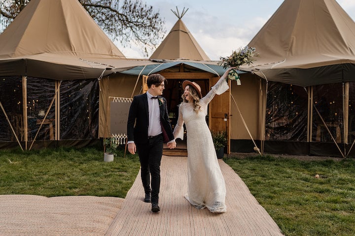 Bride and Groom walking out of the tipis holding the floral bouquet in their air looking very happy